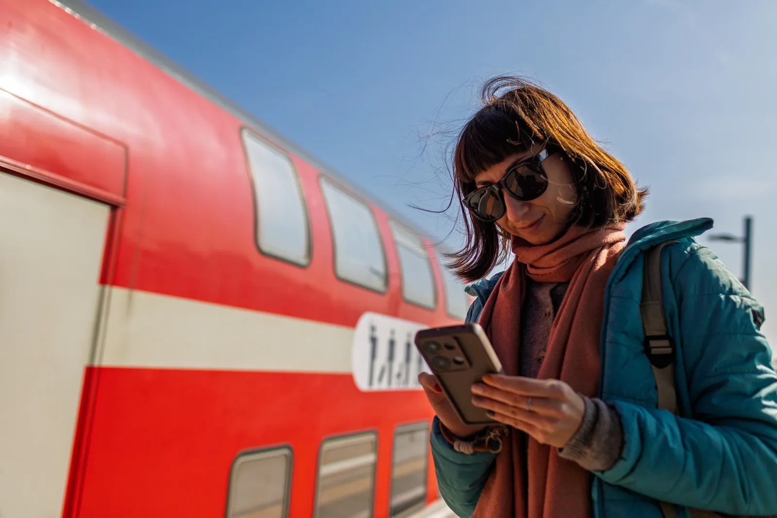 Bahnreisende steht vor einem Regionalzug der Deutschen Bahn und prüft ihr Handy