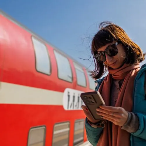 Bahnreisende steht vor einem Regionalzug der Deutschen Bahn und prüft ihr Handy