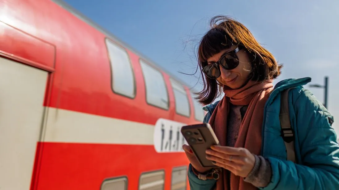 Bahnreisende steht vor einem Regionalzug der Deutschen Bahn und prüft ihr Handy