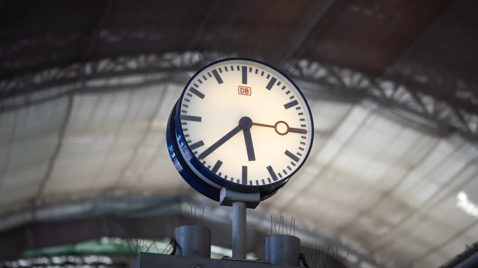 Eine Uhr der Deutschen Bahn im Vordergrund. Im Hintergrund sieht man die Decke eines Bahnhofs.