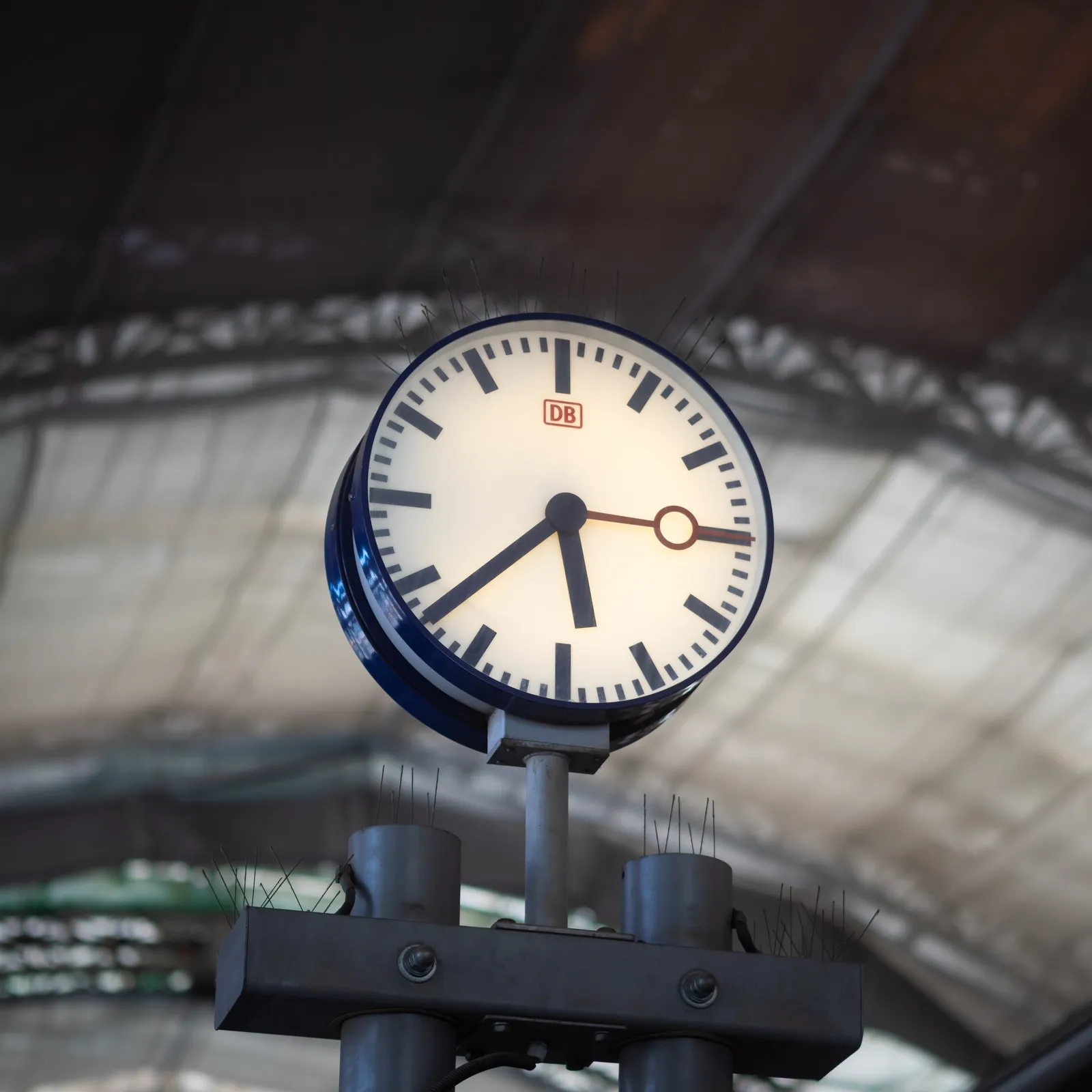 Eine Uhr der Deutschen Bahn im Vordergrund. Im Hintergrund sieht man die Decke eines Bahnhofs.