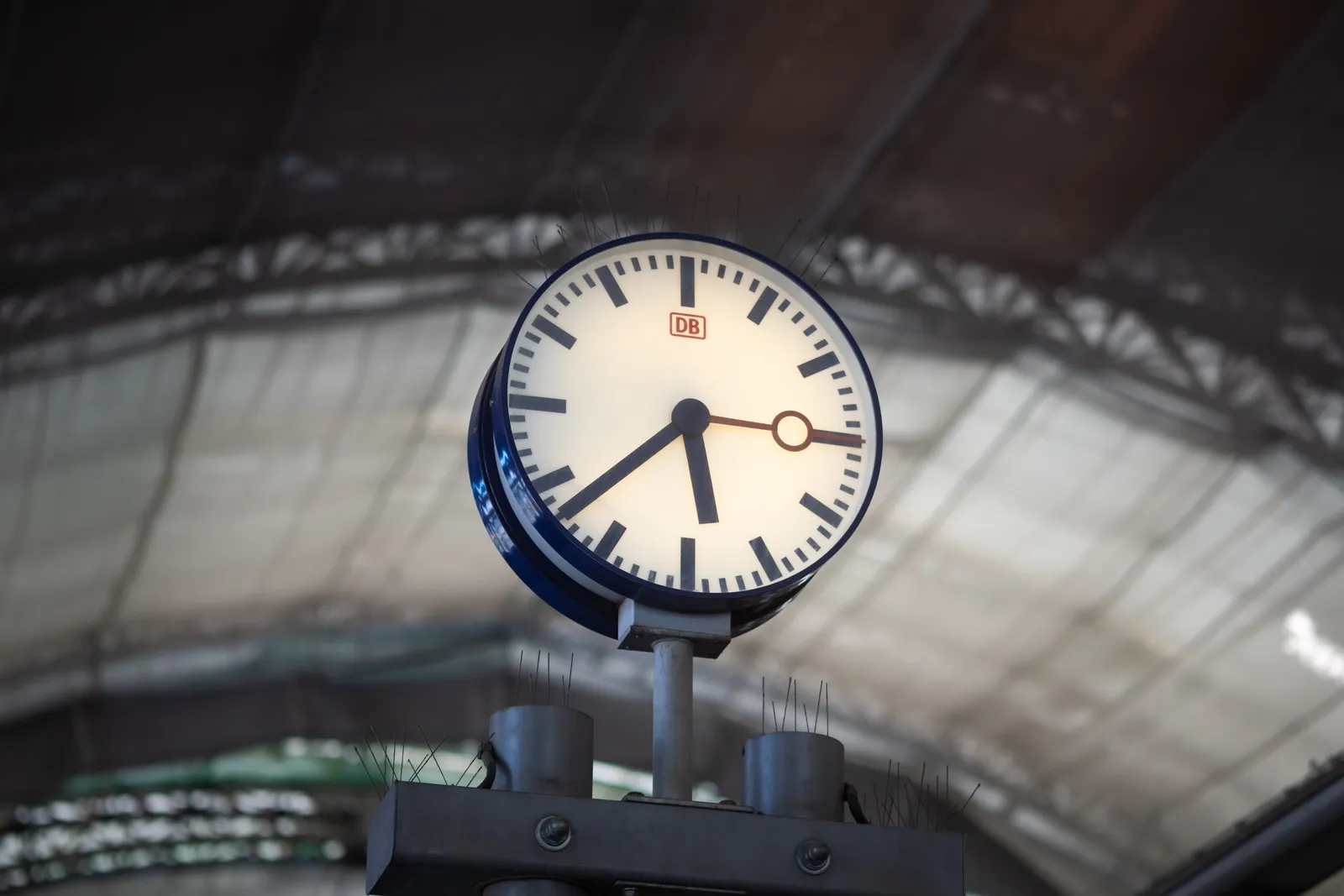 Eine Uhr der Deutschen Bahn im Vordergrund. Im Hintergrund sieht man die Decke eines Bahnhofs.
