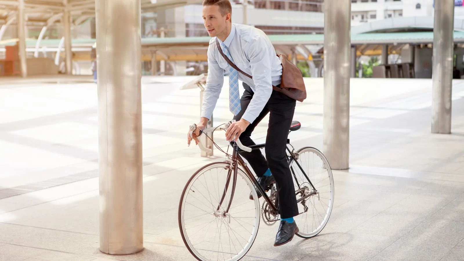 Ein Mann fährt auf einem Fahrrad an Gebäuden vorbei und trägt eine braune Arbeitstasche.