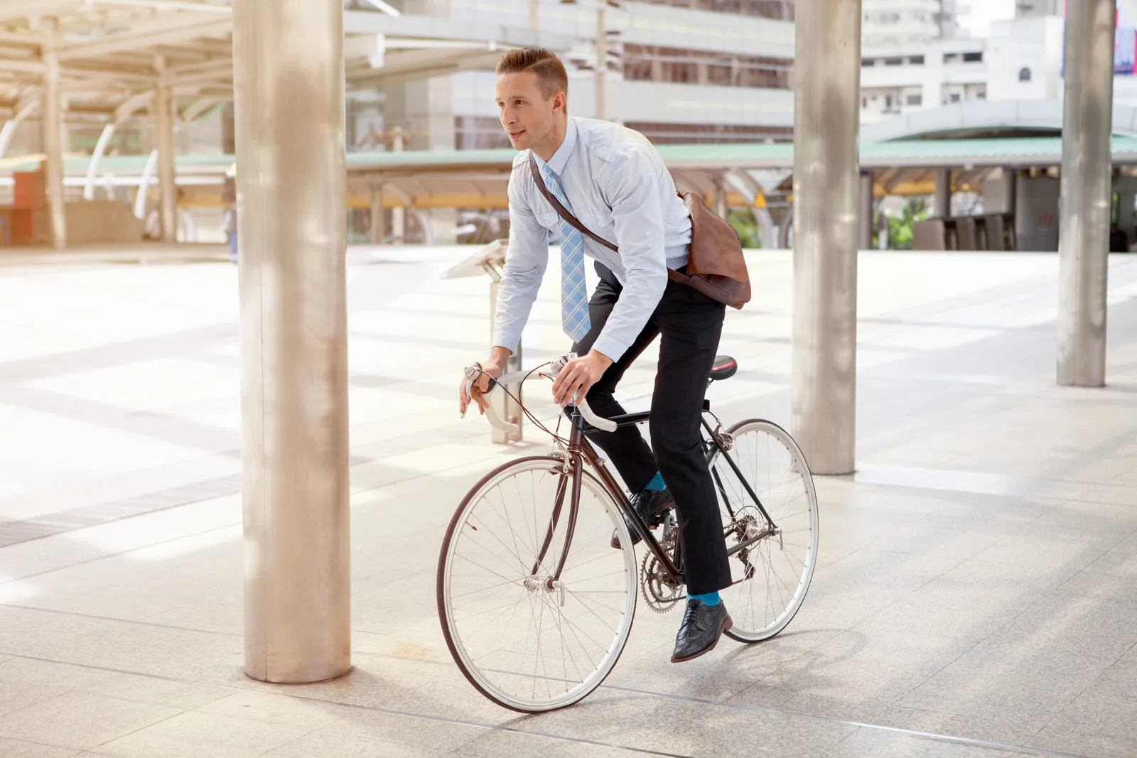 Ein Mann fährt auf einem Fahrrad an Gebäuden vorbei und trägt eine braune Arbeitstasche.