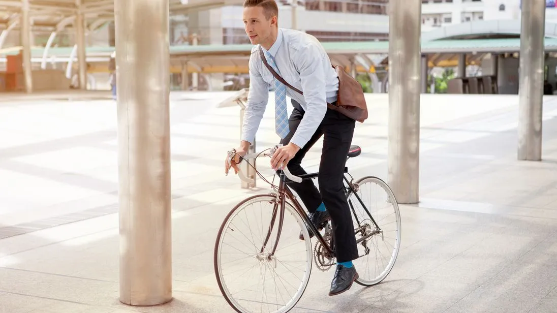 Ein Mann fährt auf einem Fahrrad an Gebäuden vorbei und trägt eine braune Arbeitstasche.