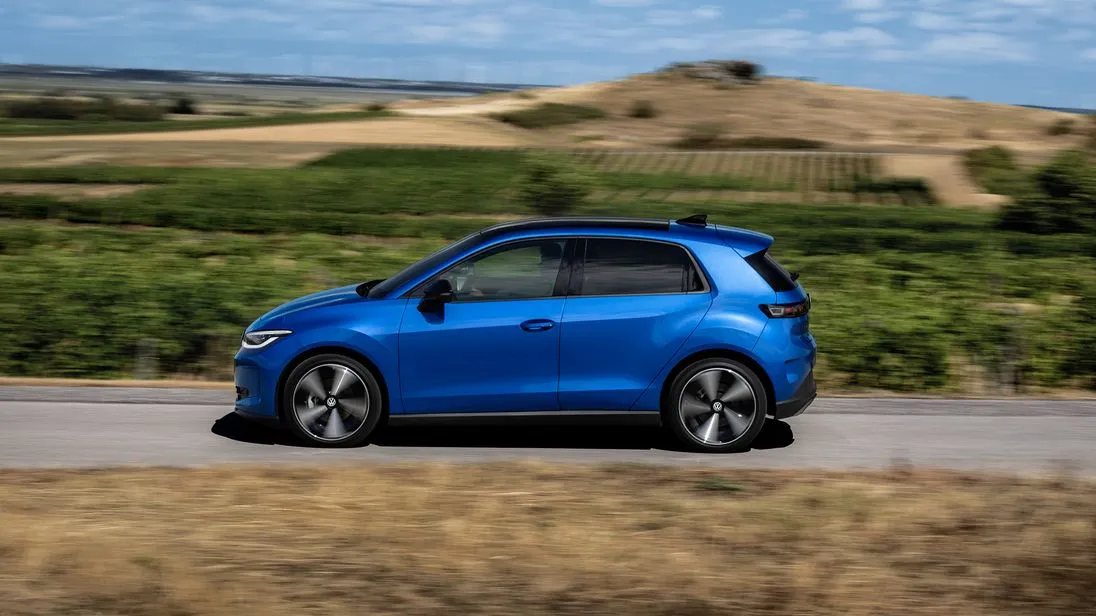 Blauer VW ID. Polo fährt auf einer schmalen Straße unter blauem Himmel.