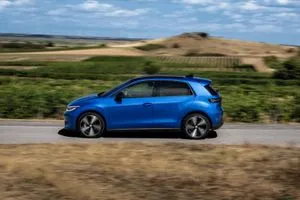 Blauer VW ID. Polo fährt auf einer schmalen Straße unter blauem Himmel.