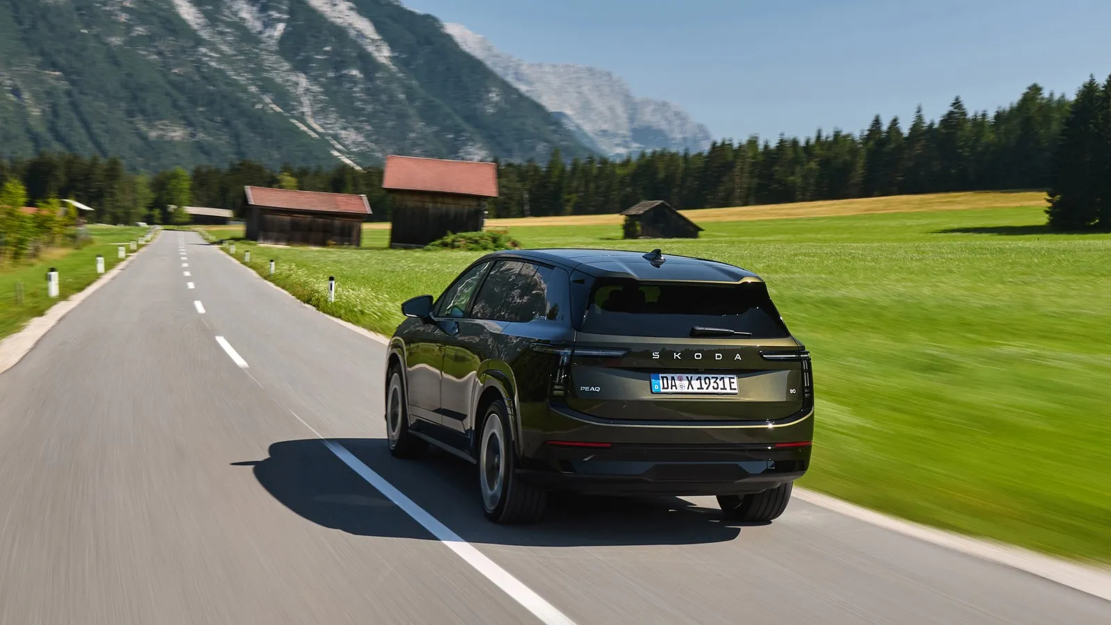 Der Skoda Peaq 90 von hinten vor grünen Bergwiesen und hohen Bergen.