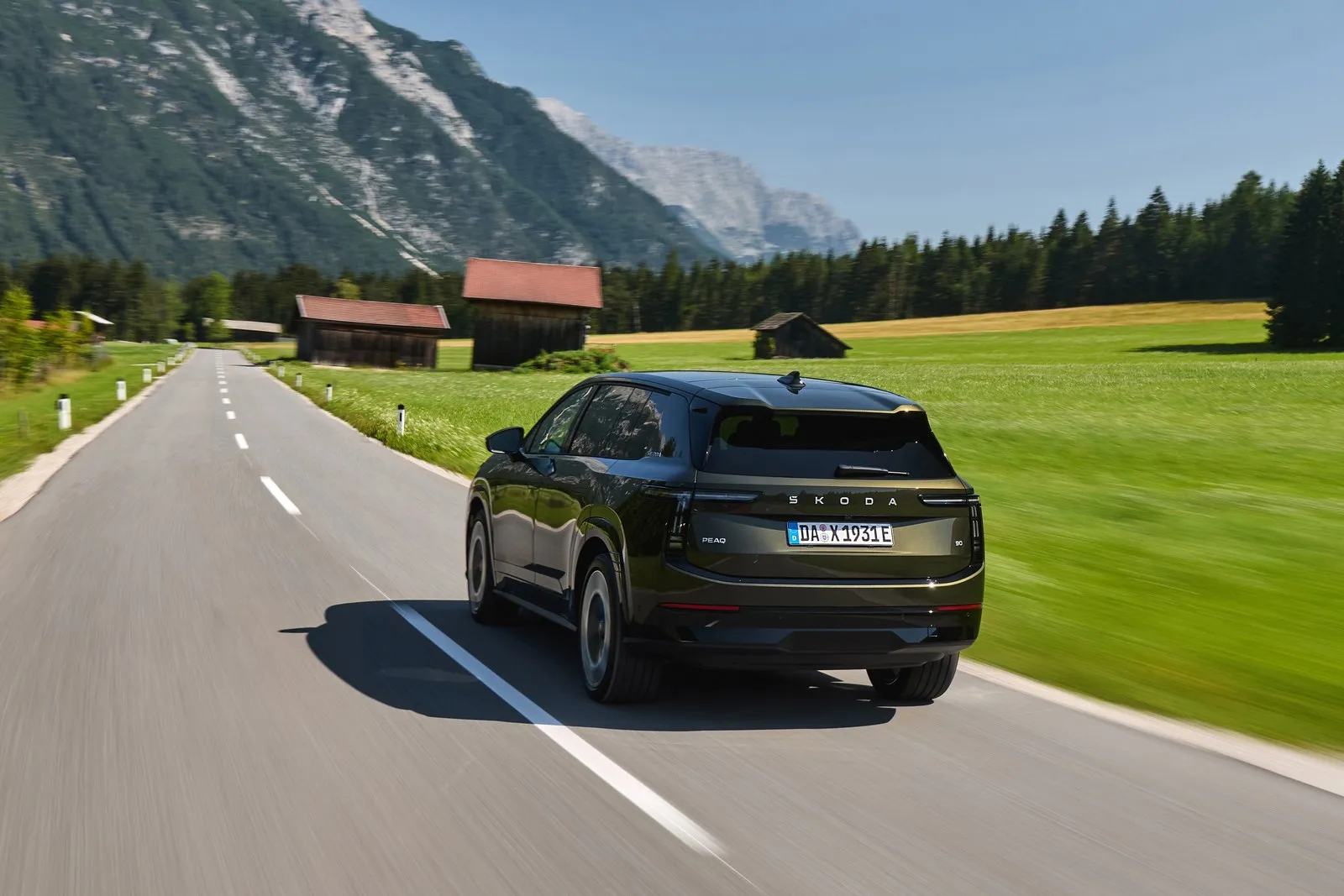 Der Skoda Peaq 90 von hinten vor grünen Bergwiesen und hohen Bergen.