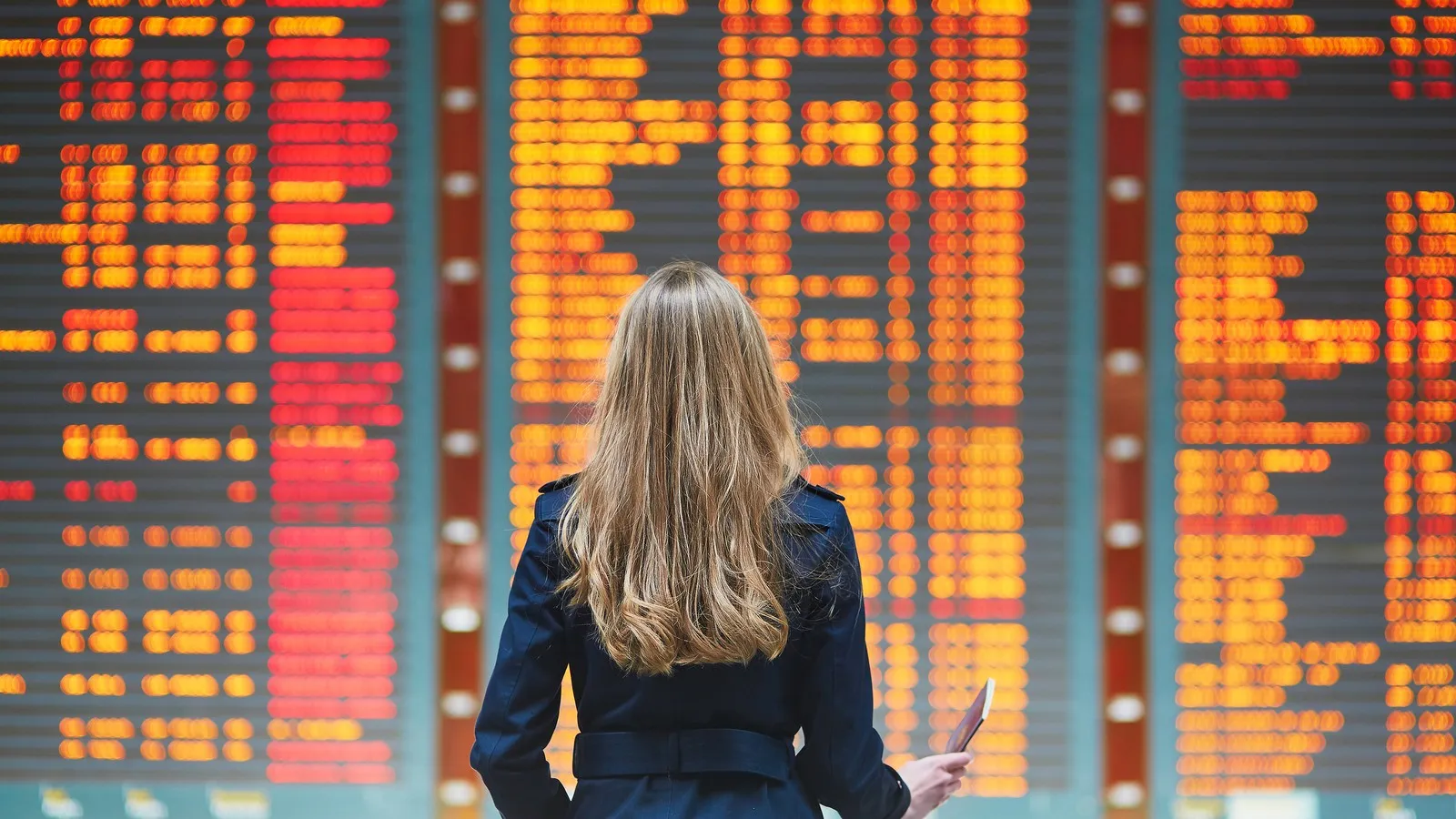 Eine junge Frau betrachtet den Abflugplan an einem Flughafen.