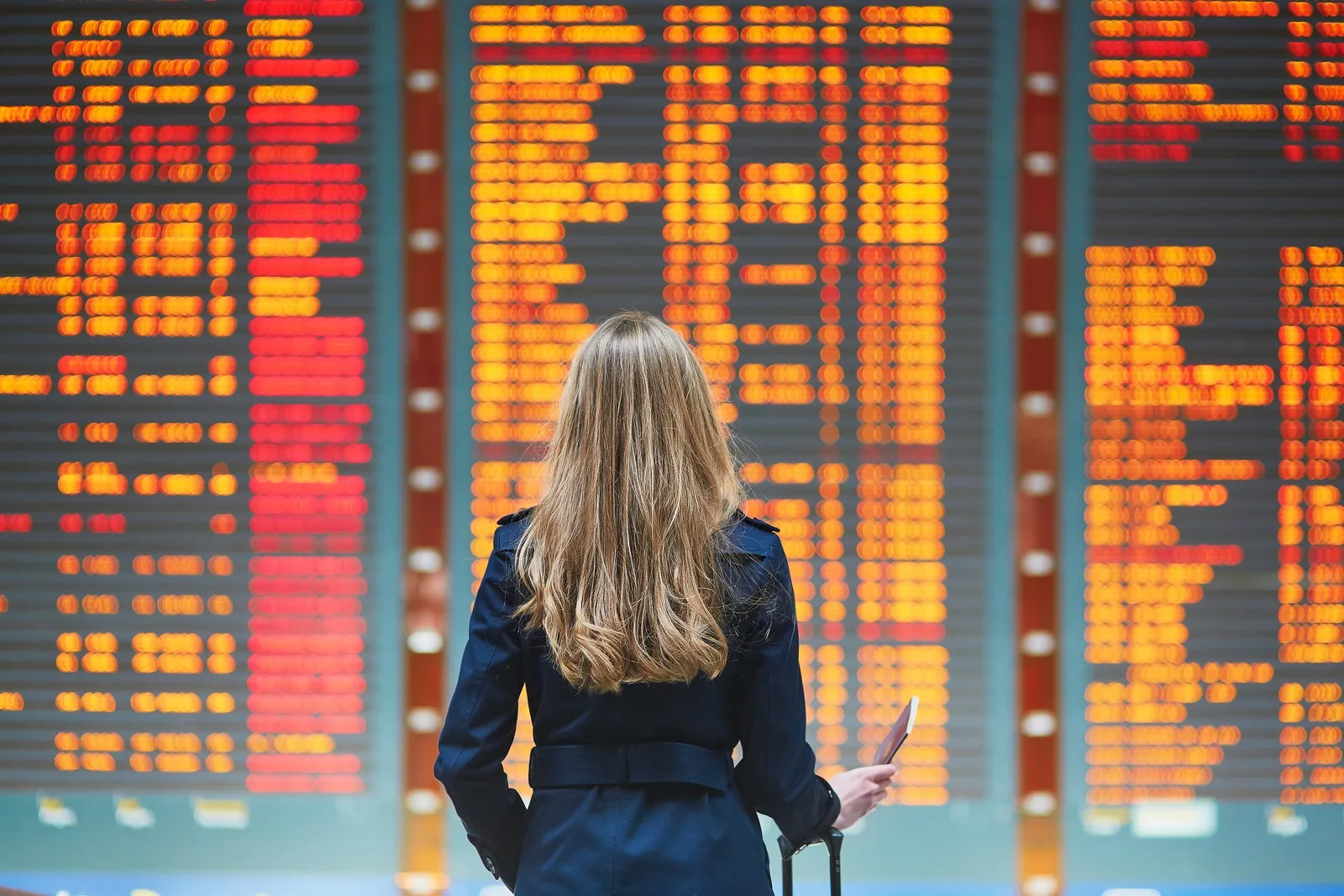 Eine junge Frau betrachtet den Abflugplan an einem Flughafen.