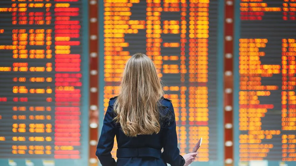 Eine junge Frau betrachtet den Abflugplan an einem Flughafen.