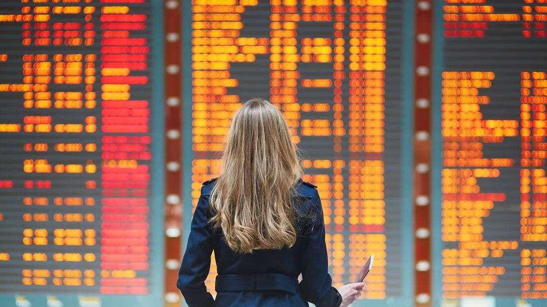 Eine junge Frau betrachtet den Abflugplan an einem Flughafen.