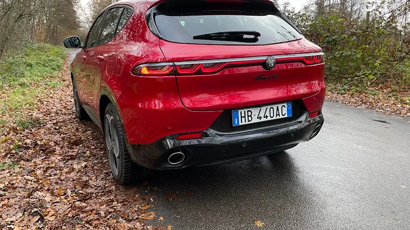 Roter Alfa Romeo Tonale von hinten auf nasser Straße am Waldrand.
