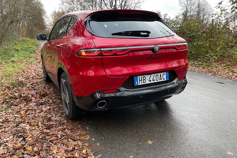 Roter Alfa Romeo Tonale von hinten auf nasser Straße am Waldrand.