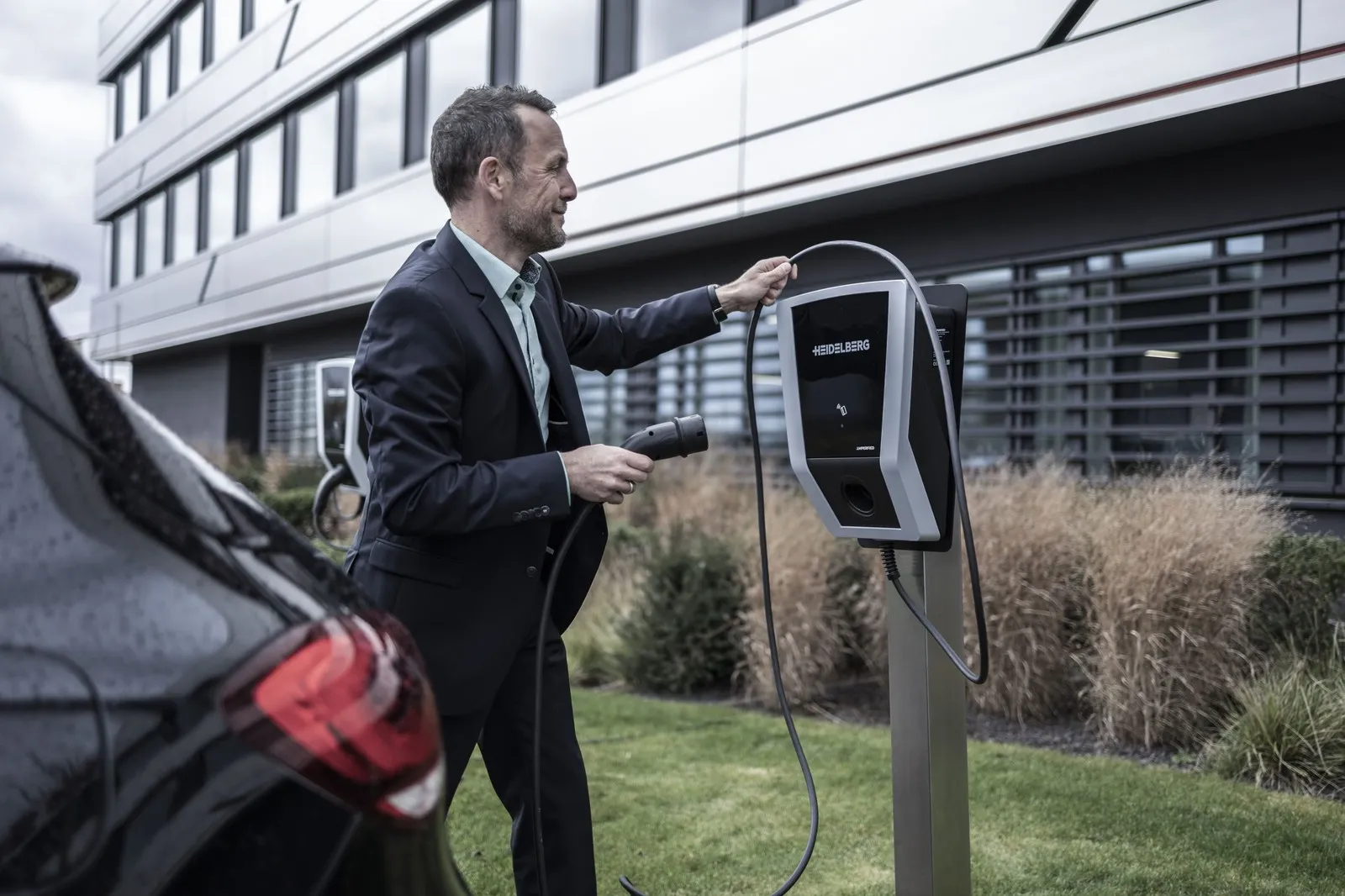 Ein Mann schließt ein Elektroauto an einer Ladesäule vor einem Firmengebäude an.