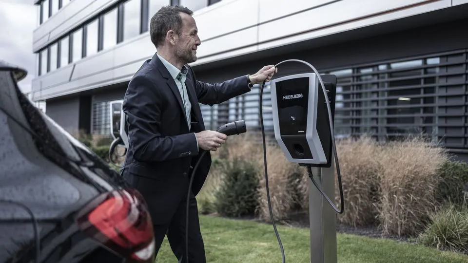 Ein Mann schließt ein Elektroauto an einer Ladesäule vor einem Firmengebäude an.
