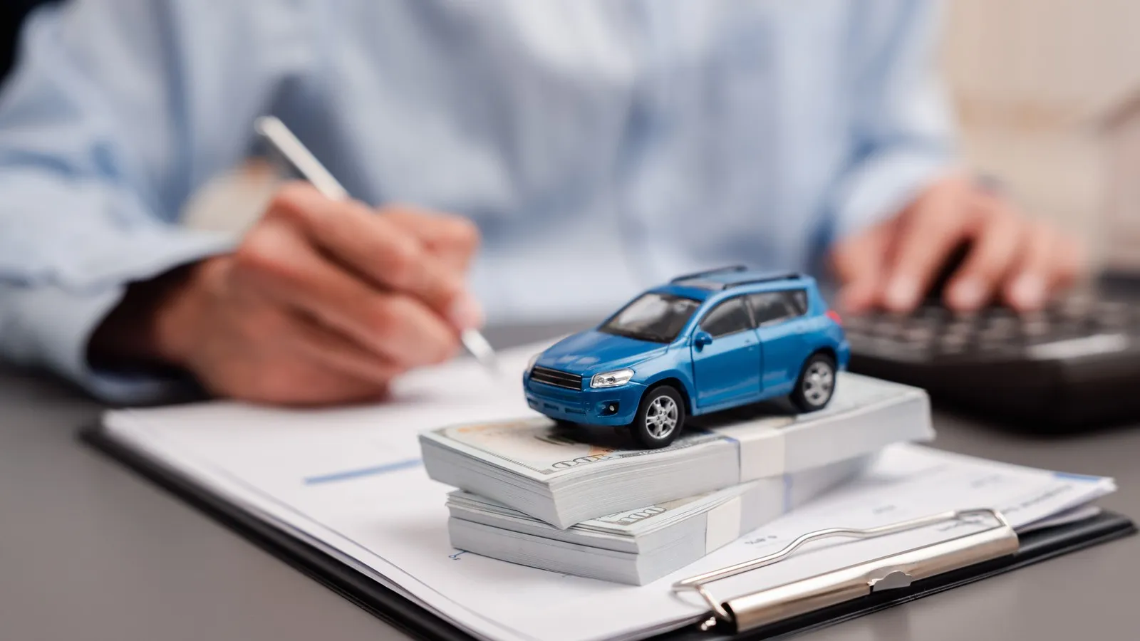 Eine Person schreibt mit einem Stift auf einem Leasing-Vertrag. Ein blaues Spielzeugauto steht davor auf dem Tisch.