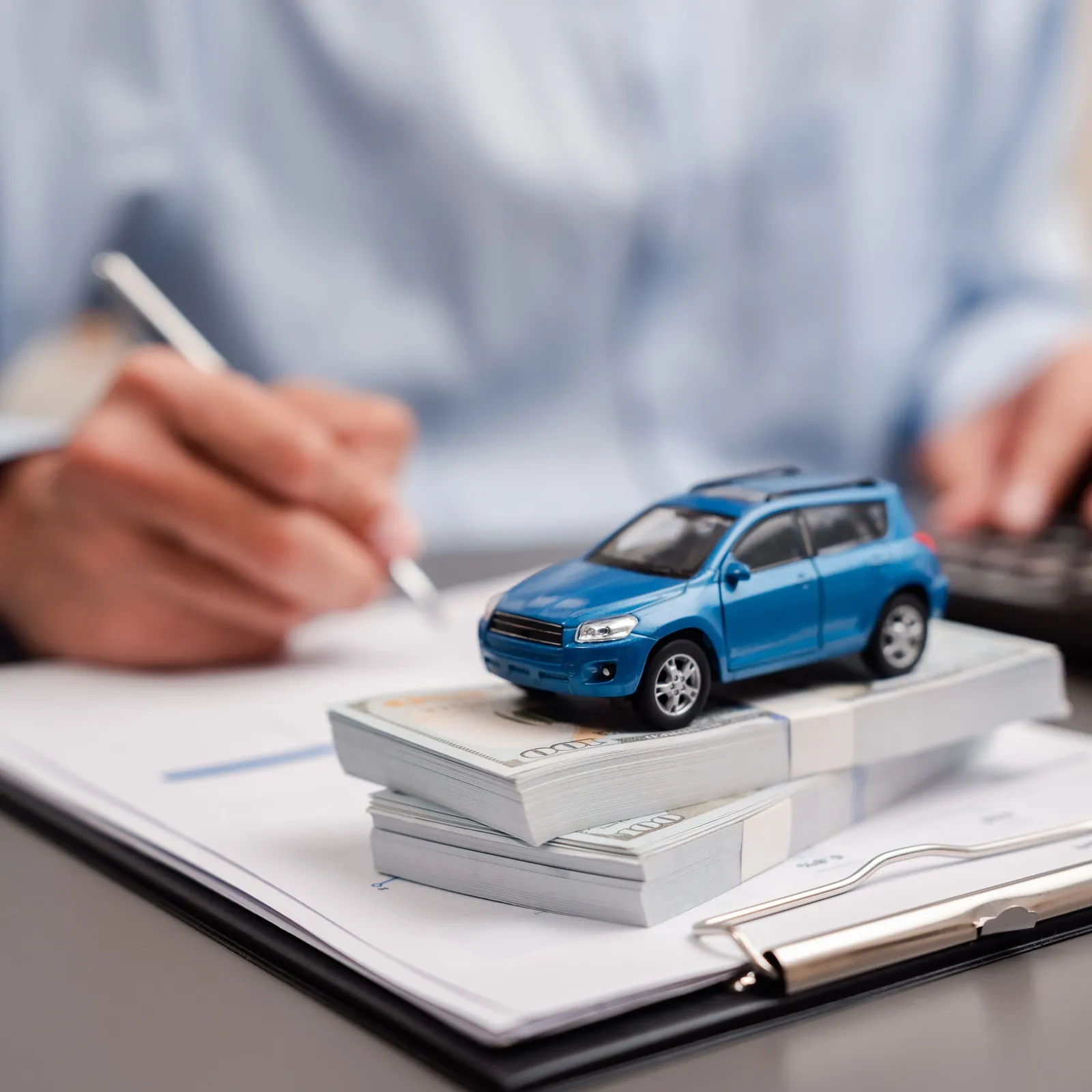 Eine Person schreibt mit einem Stift auf einem Leasing-Vertrag. Ein blaues Spielzeugauto steht davor auf dem Tisch.