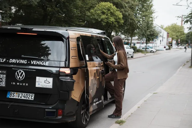 Autonomer VW ID. Buzz von Moia steht am Straßenrand, während eine Frau an der geöffneten Schiebetür einsteigt.