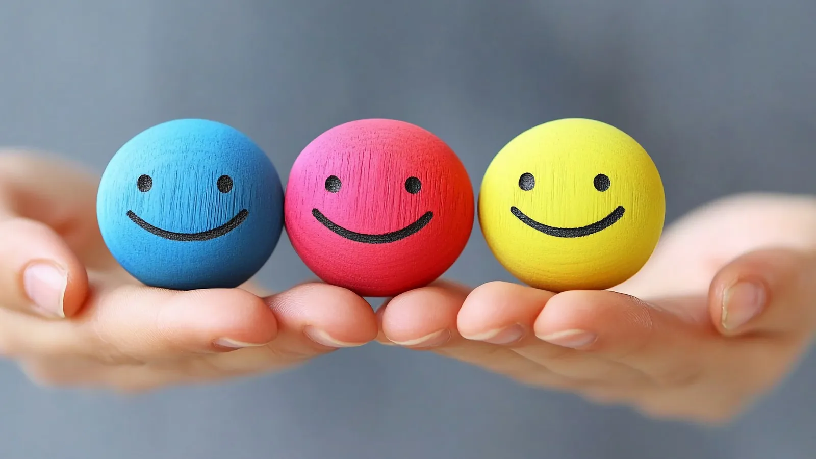 Zwei Hände die drei Smileys halten: ein blauer, ein roter und ein gelber. Die Smileys lächeln.