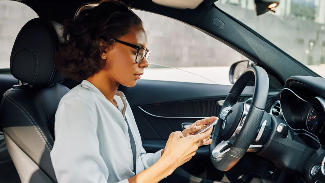 Frau im Auto tippt auf ihrem Handy.