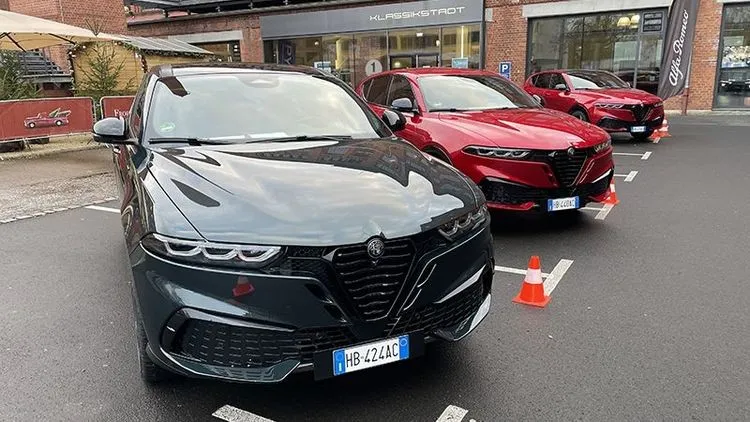 Zwei Alfa Romeo Tonale stehen vor einem Autohaus, vorne ein dunkles Modell und dahinter ein rotes Modell.