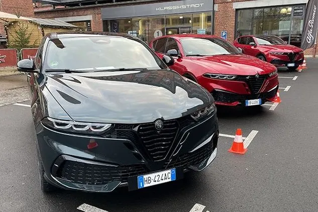 Zwei Alfa Romeo Tonale stehen vor einem Autohaus, vorne ein dunkles Modell und dahinter ein rotes Modell.