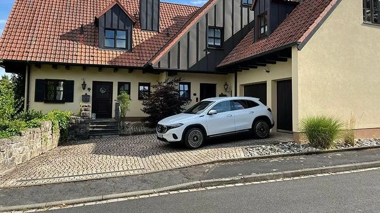Der Mercedes EQA in weiß steht vor einem Familienhaus.