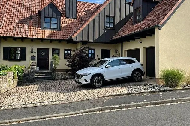 Der Mercedes EQA in weiß steht vor einem Familienhaus.