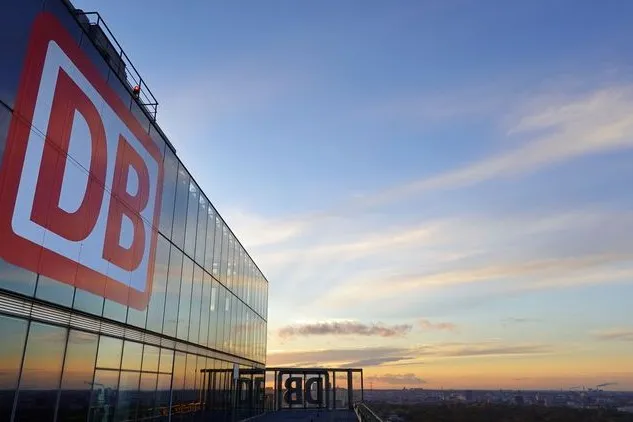 DB-Logo an der Glasfassade eines Bürogebäudes bei Sonnenuntergang.