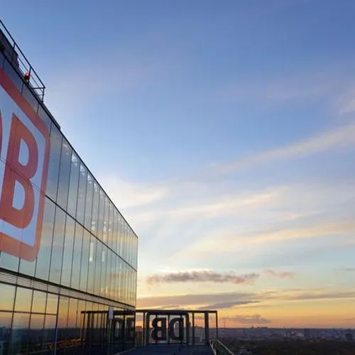 DB-Logo an der Glasfassade eines Bürogebäudes bei Sonnenuntergang.