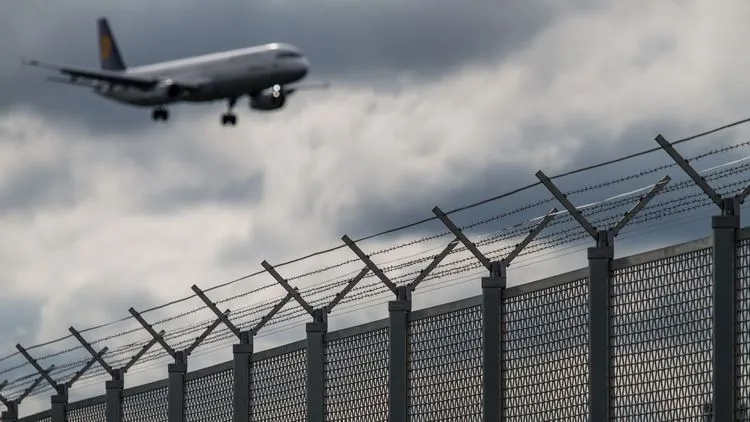 Flugzeug im Landeanflug hinter Sicherheitszaun eines Flughafens.