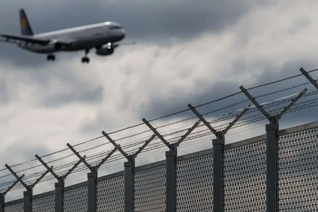 Flugzeug im Landeanflug hinter Sicherheitszaun eines Flughafens.