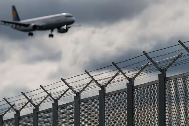 Flugzeug im Landeanflug hinter Sicherheitszaun eines Flughafens.