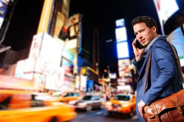 Businessmann telefoniert in New York (Manhattan) und läuft dabei die vollbefahrene Straße entlang.