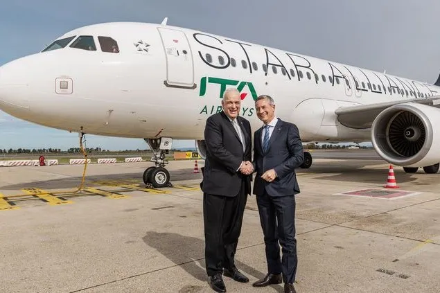 Zwei Männer in Anzügen stehen auf dem Rollfeld vor einem Flugzeug von ITA Airways und geben sich die Hand. Das Passagierflugzeug trägt die Lackierung der Star Alliance.