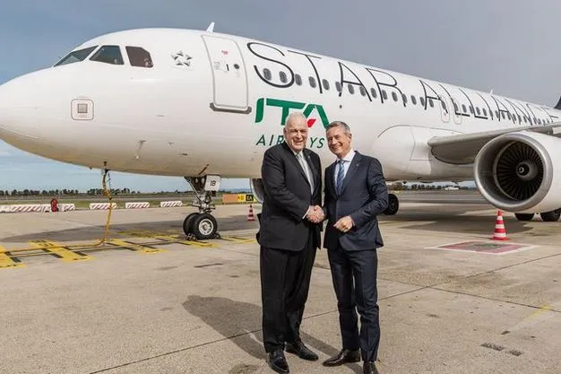 Zwei Männer in Anzügen stehen auf dem Rollfeld vor einem Flugzeug von ITA Airways und geben sich die Hand. Das Passagierflugzeug trägt die Lackierung der Star Alliance.