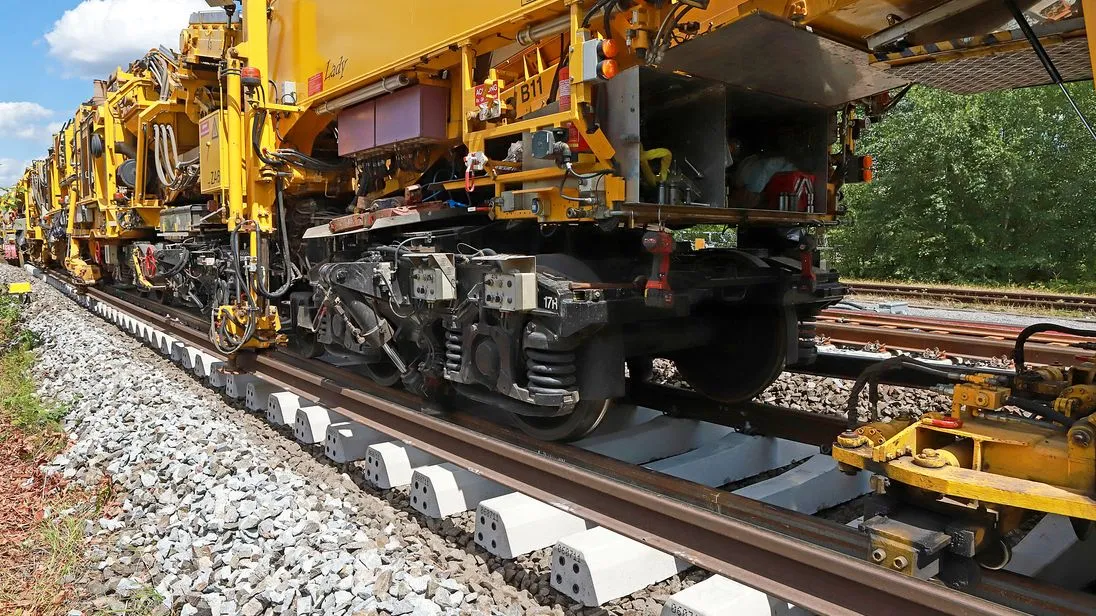 Gelbe Gleisbaumaschine bei Arbeiten an einer Bahnstrecke mit neu verlegten Betonschwellen und Schienen.