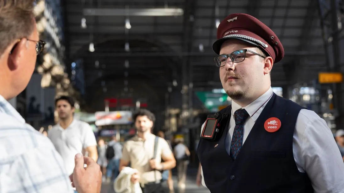 Mitarbeiter des Bahnhofsservice der DB mit Bodycam im Gespräch mit einem Reisenden am Hauptbahnhof Frankfurt (Main)