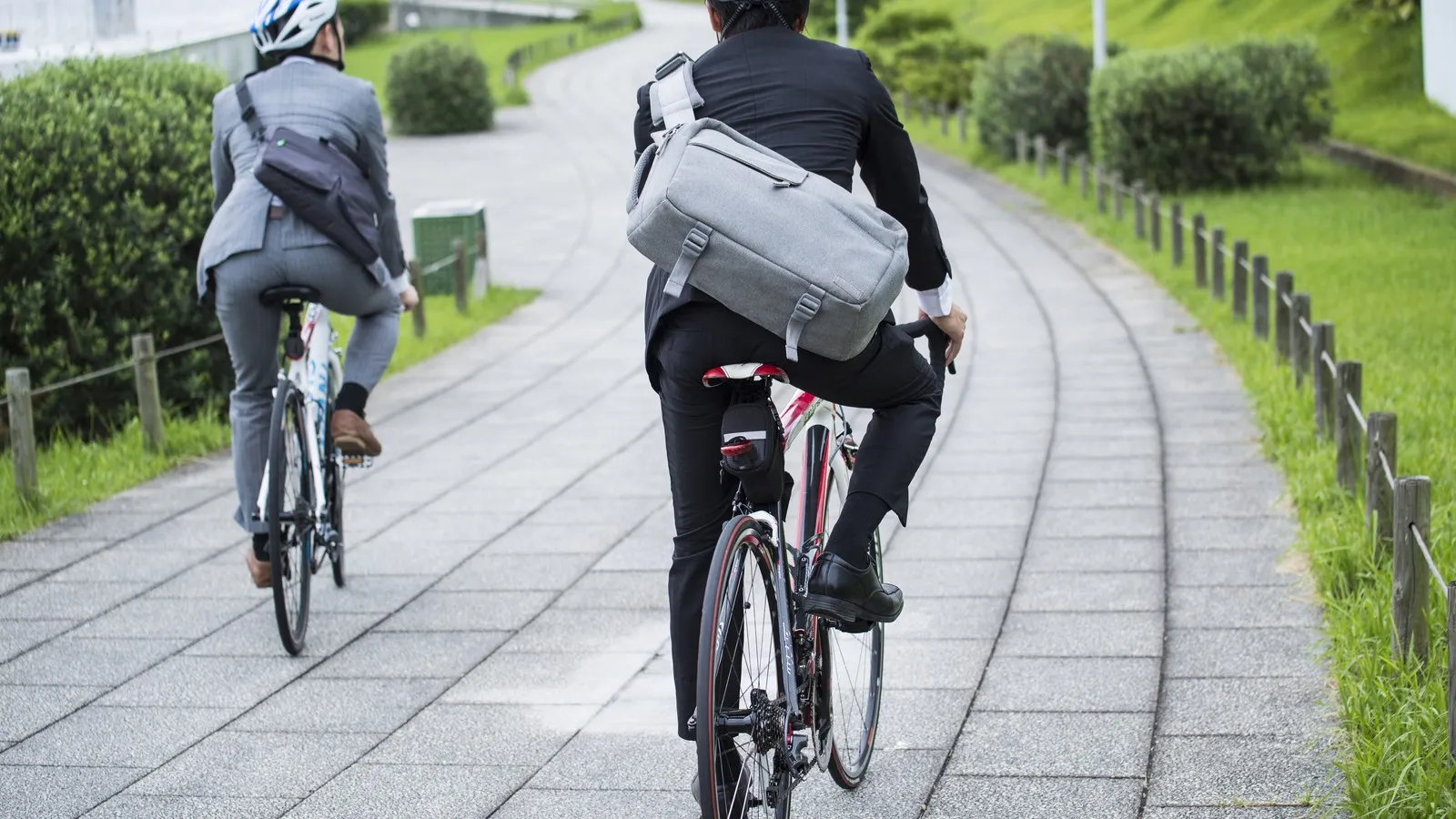 Zwei Männer im Anzug und mit Fahrradhelm und Umhängetasche auf dem Weg zur Arbeit auf dem Fahrrad