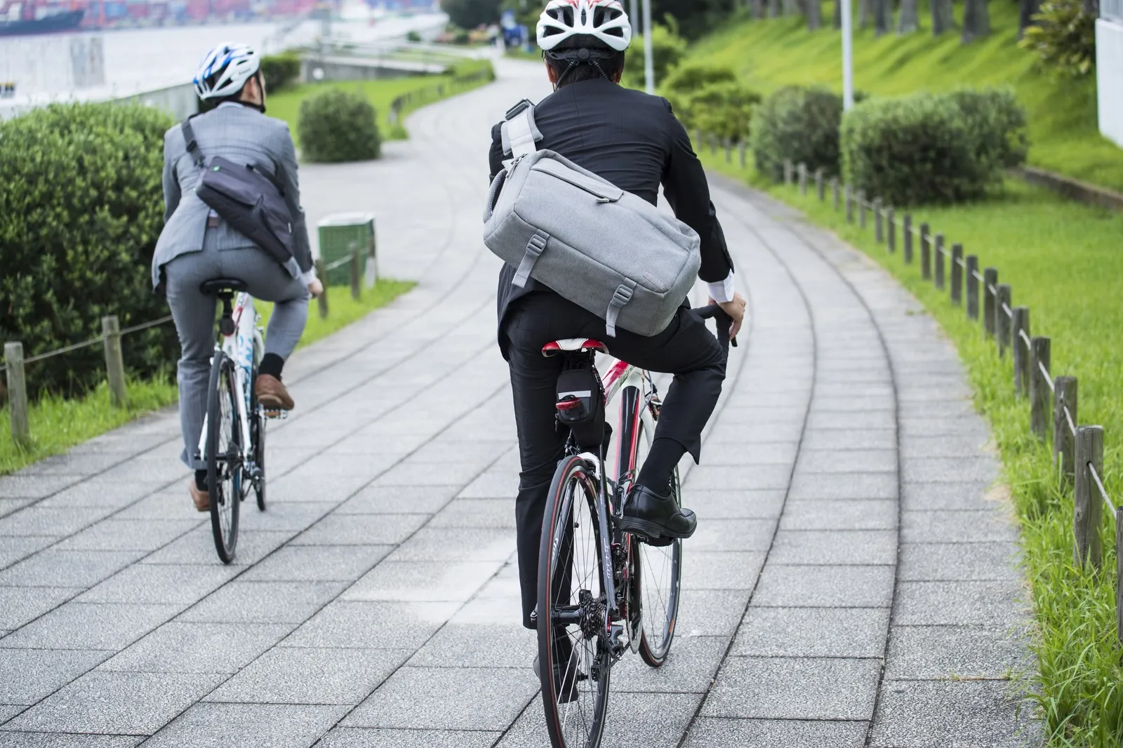 Zwei Männer im Anzug und mit Fahrradhelm und Umhängetasche auf dem Weg zur Arbeit auf dem Fahrrad
