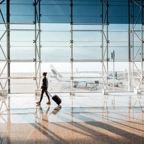 Eine Person mit Rollkoffer geht durch ein helles Flughafenterminal. Durch die große Glasfront sind Flugzeuge auf dem Vorfeld zu sehen.