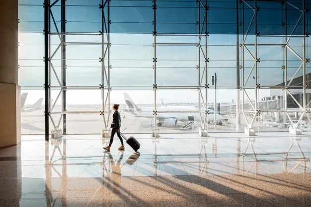 Eine Person mit Rollkoffer geht durch ein helles Flughafenterminal. Durch die große Glasfront sind Flugzeuge auf dem Vorfeld zu sehen.