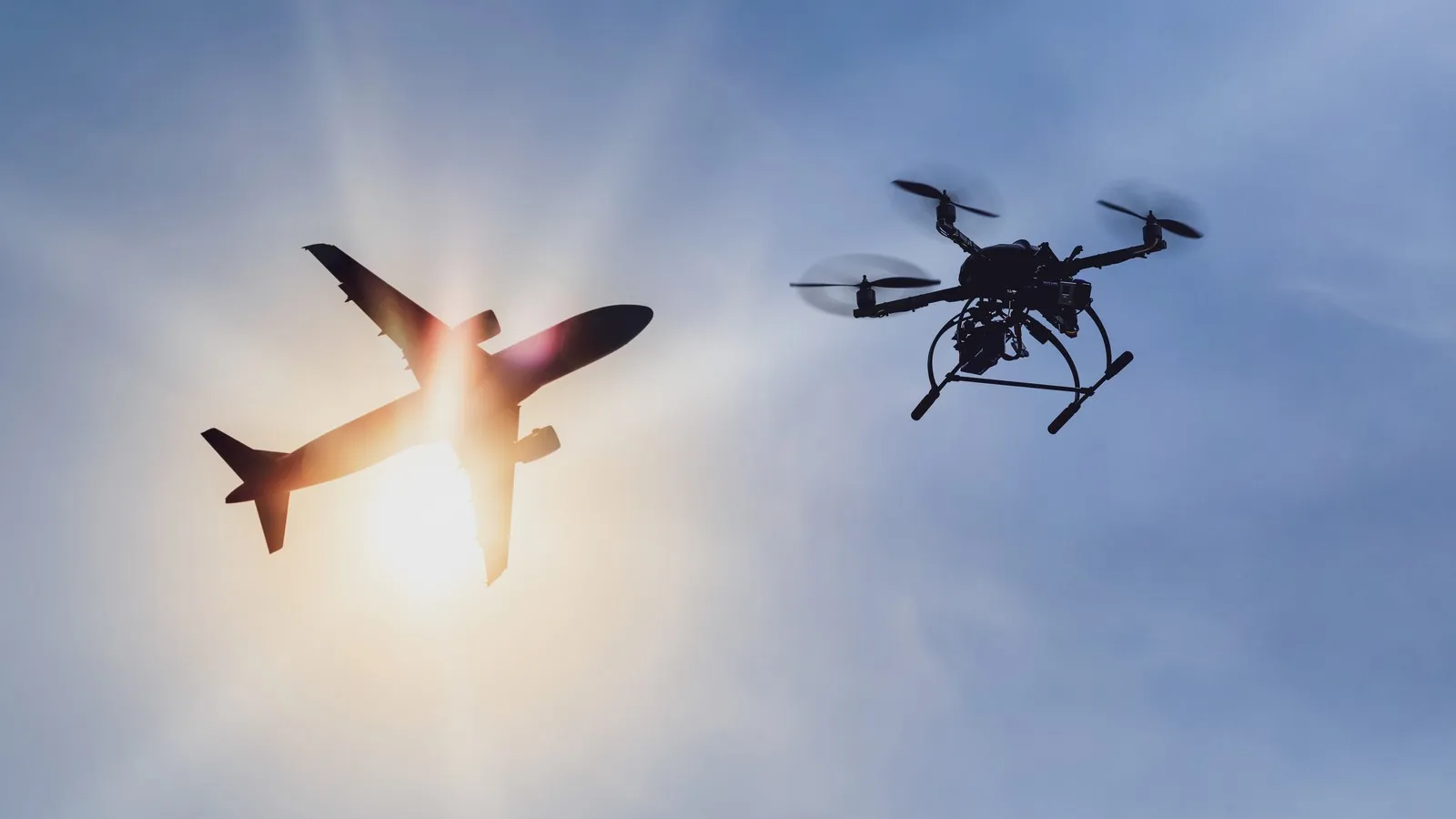 Im Vordergrund ist eine fliegene Drohne vor einem in den Himmel fliegenden Flugzeug.