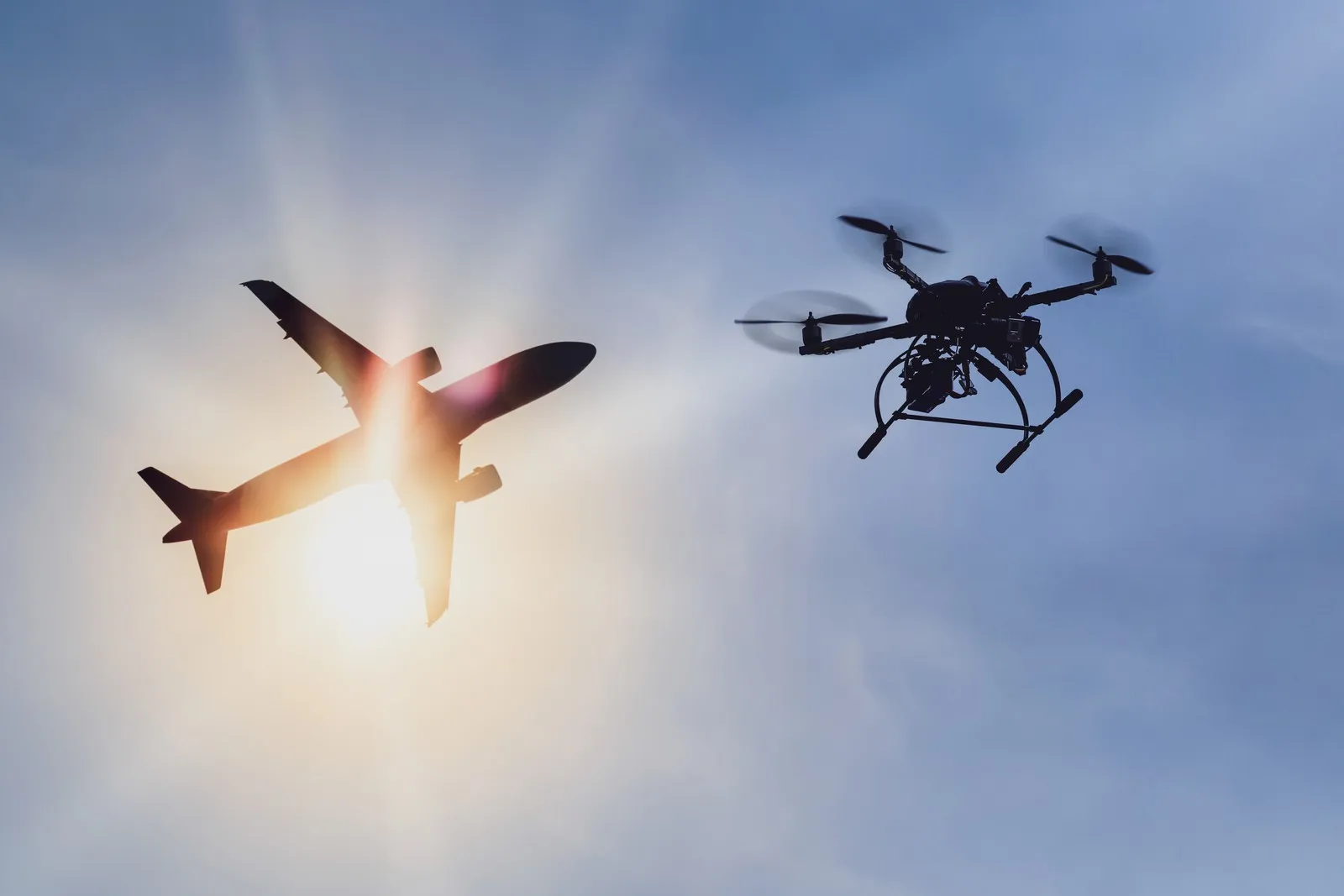 Im Vordergrund ist eine fliegene Drohne vor einem in den Himmel fliegenden Flugzeug.