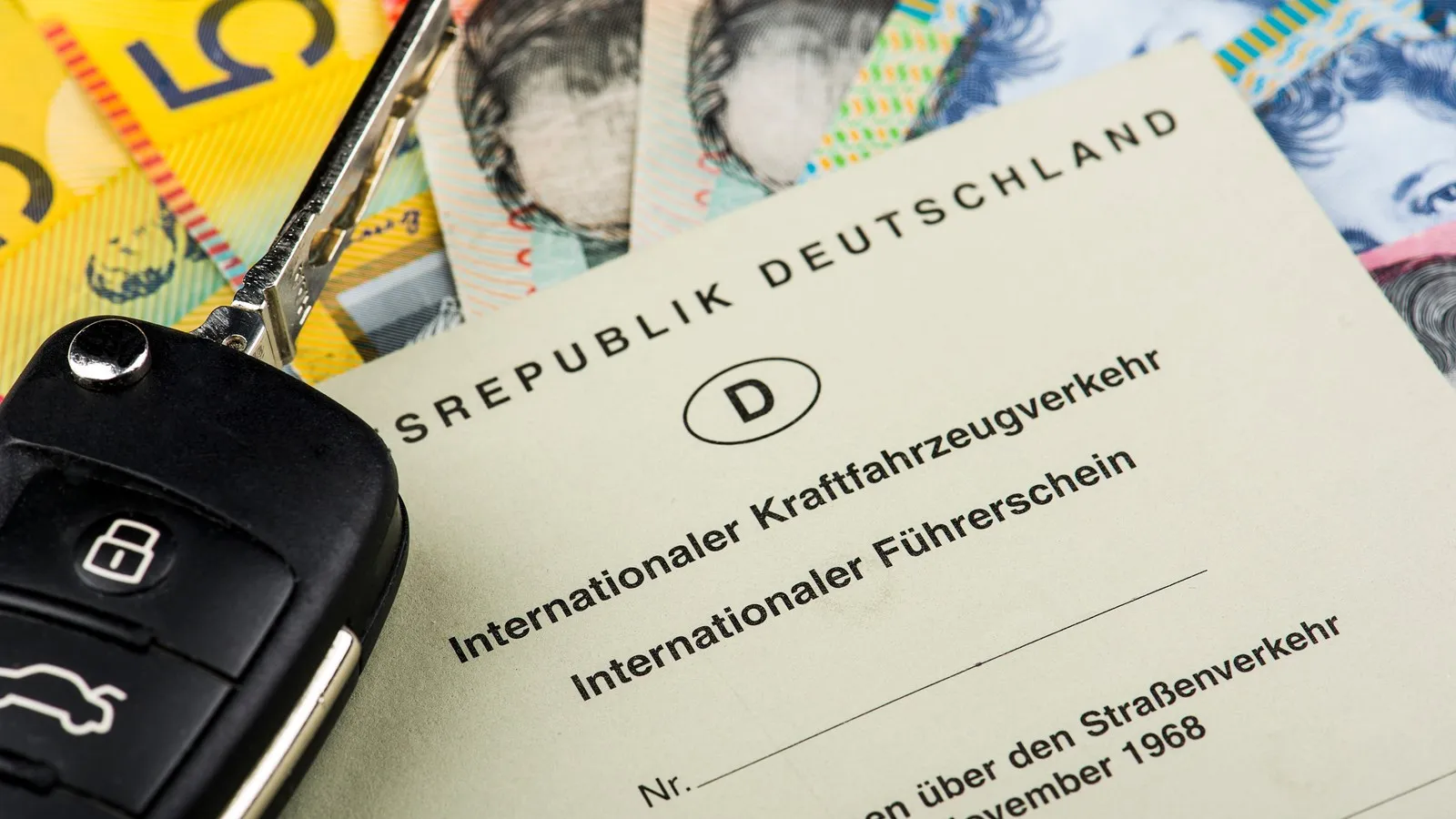 Internationaler Führerschein der Bundesrepublik Deutschland liegt auf mehreren Geldscheinen neben einem Autoschlüssel.