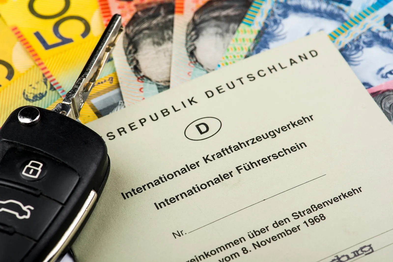 Internationaler Führerschein der Bundesrepublik Deutschland liegt auf mehreren Geldscheinen neben einem Autoschlüssel.