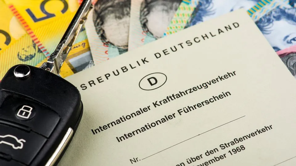 Internationaler Führerschein der Bundesrepublik Deutschland liegt auf mehreren Geldscheinen neben einem Autoschlüssel.