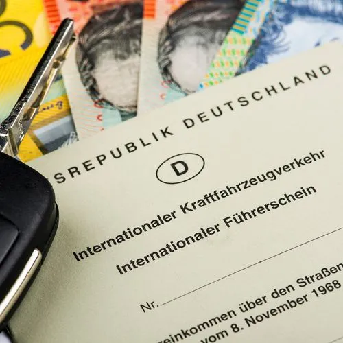 Internationaler Führerschein der Bundesrepublik Deutschland liegt auf mehreren Geldscheinen neben einem Autoschlüssel.